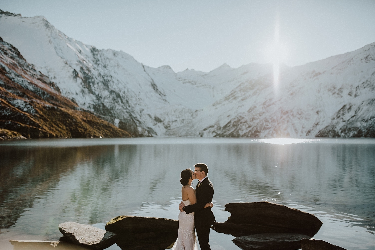 Newly wed couple kiss in front of a snowcapped mount top lake fresh fron their Queenstown elopement.