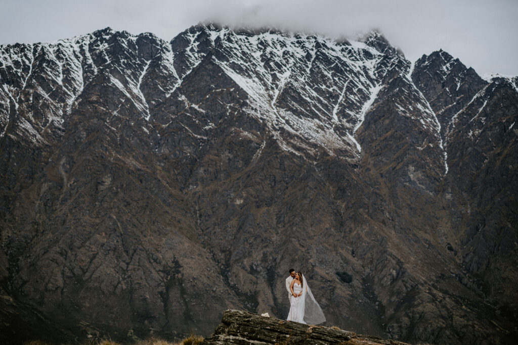 Couple in wedding outfit standing infront of a snow capped dramatic mountain range