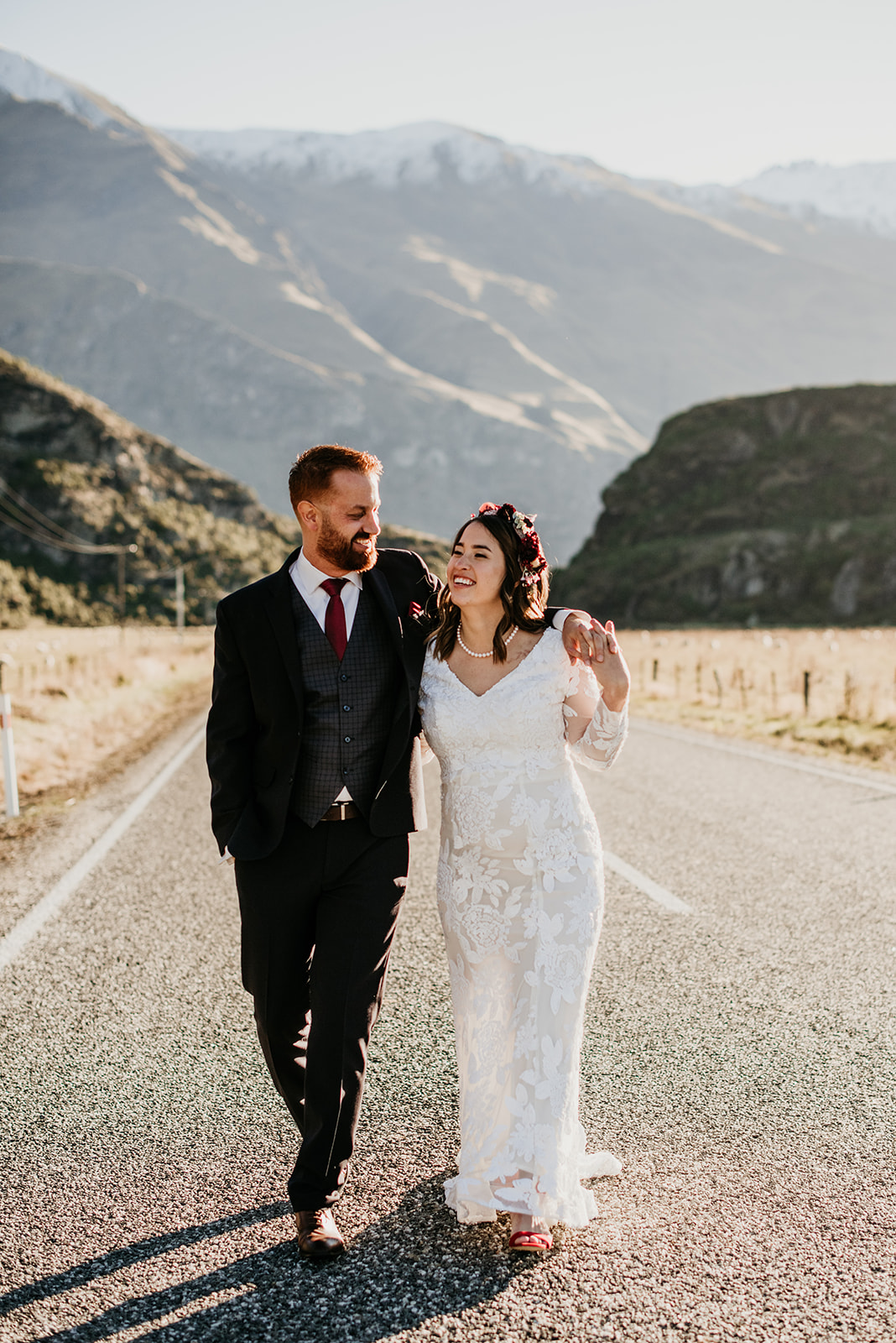 Couple in their wedding outfits holding each other walking down the middle of a desserted road looking into each others eyes