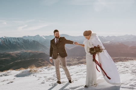 Queenstown Elopements- Couple stading o n the snow covered hills high above the township celebrating their wedding day.